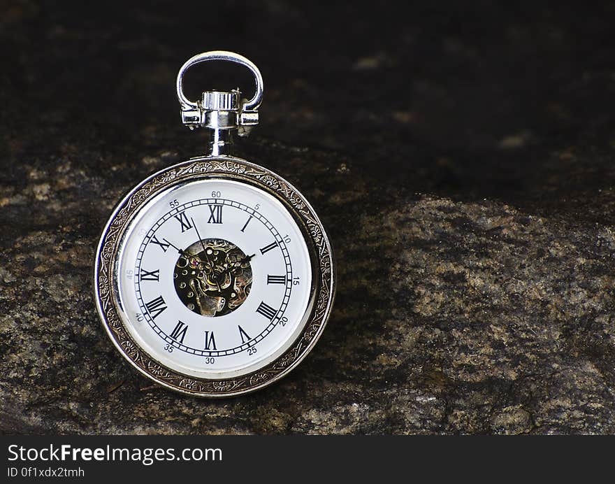 A close up of an ornamental analog watch on a rocky background.