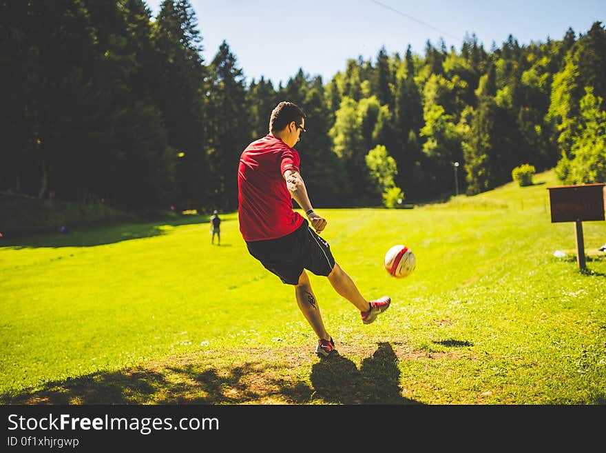 Man in Red T Shirt Playing Soccer during Daytime