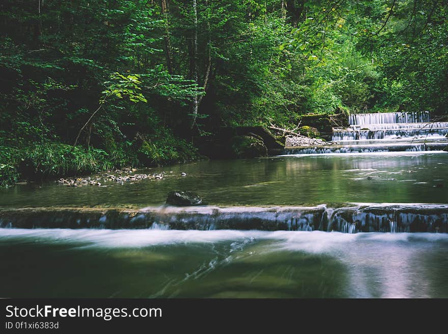 Wide river with waterfalls flowing through leafy green forest. Wide river with waterfalls flowing through leafy green forest.