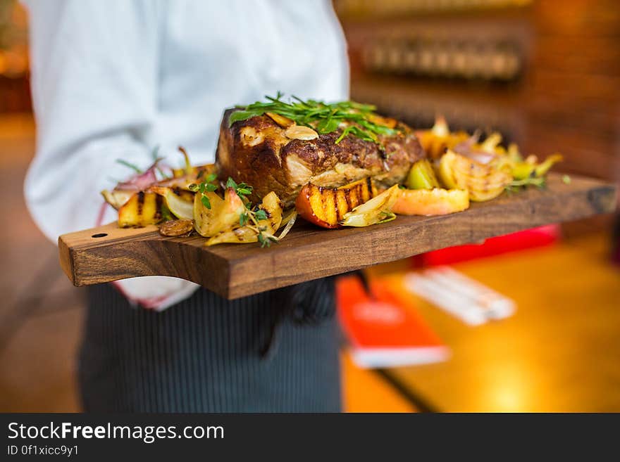 A chef serving a wood tray with roasted meat.