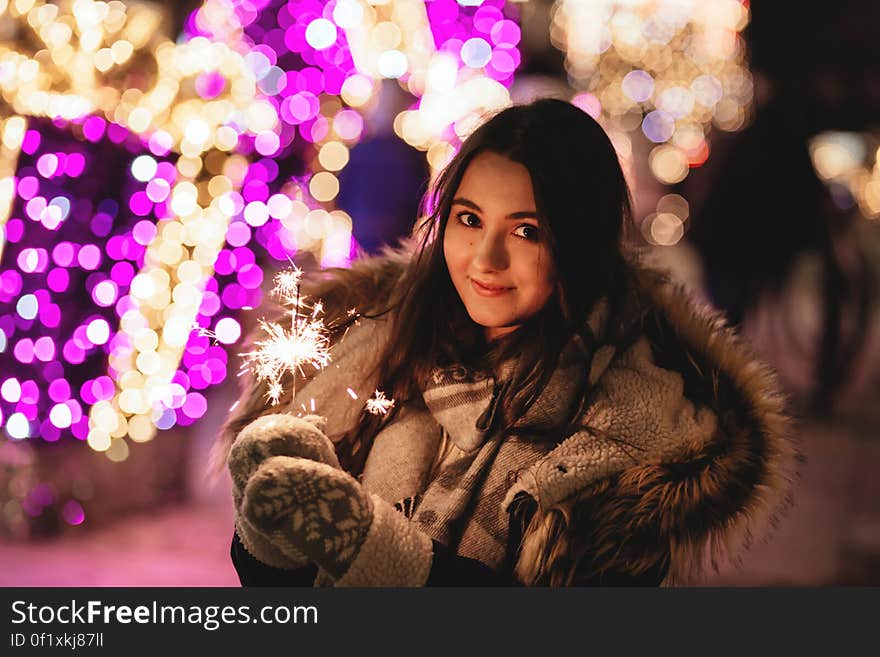 A portrait of a young woman in winter clothes holding a sparkler. A portrait of a young woman in winter clothes holding a sparkler.