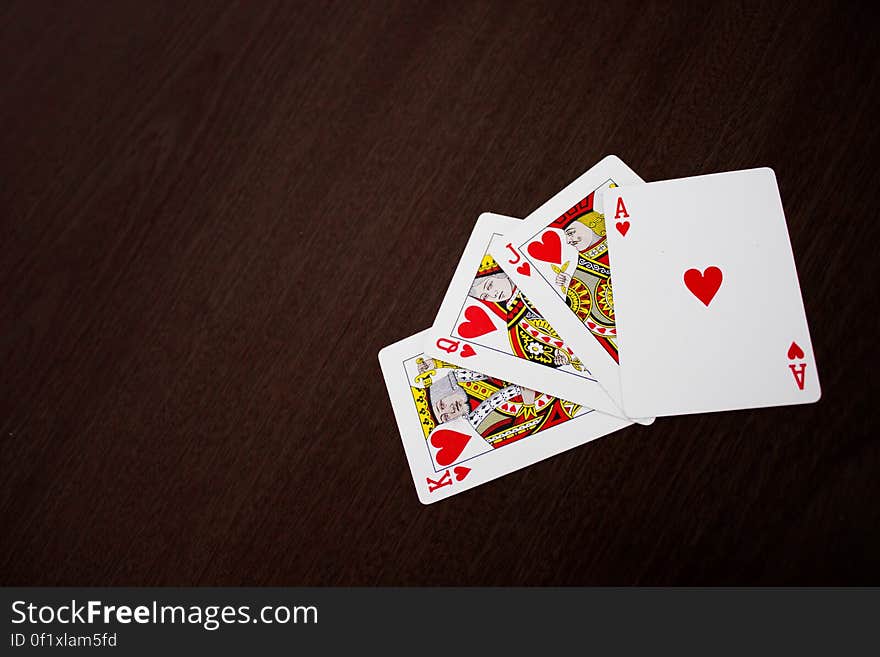 Playing cards with Ace, Jack, Queen and King of Hearts fanned out on a dark background.