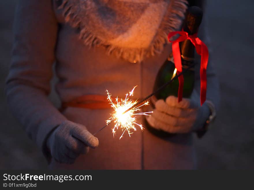 A close up of a person in winter clothes holding a bottle of champagne and a sparkler. A close up of a person in winter clothes holding a bottle of champagne and a sparkler.