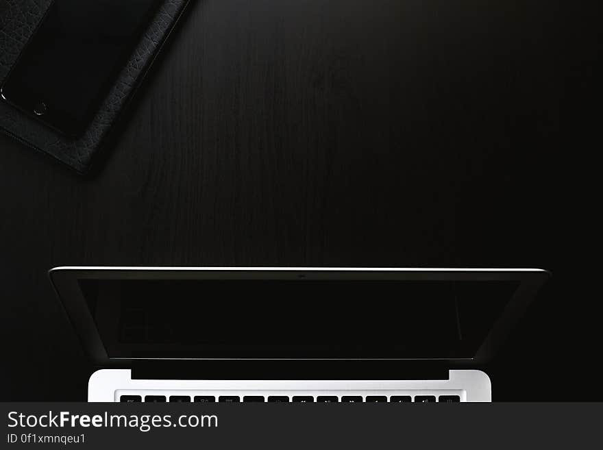 The monitor of a switched off laptop and a smartphone next to it on a black table. The monitor of a switched off laptop and a smartphone next to it on a black table.