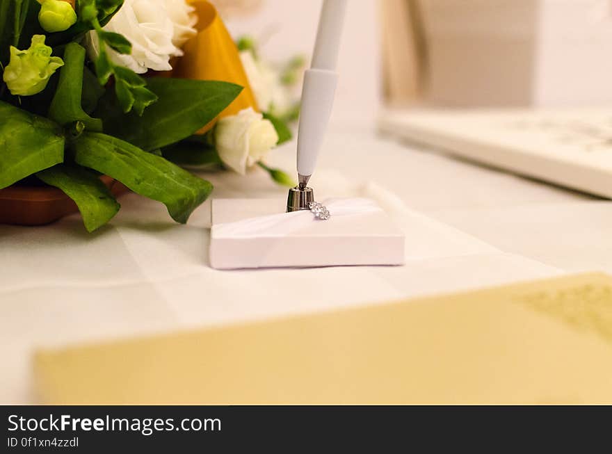 A flower arrangement with white roses and an elegant white pen next to it. A flower arrangement with white roses and an elegant white pen next to it.