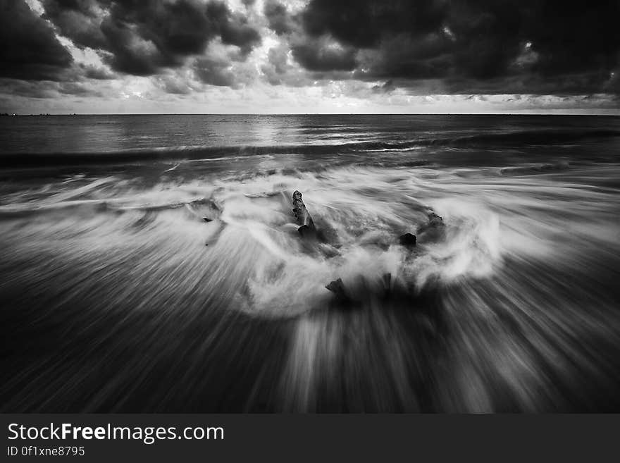 A monochrome photo of splashy waves on a beach and dark clouds above. A monochrome photo of splashy waves on a beach and dark clouds above.