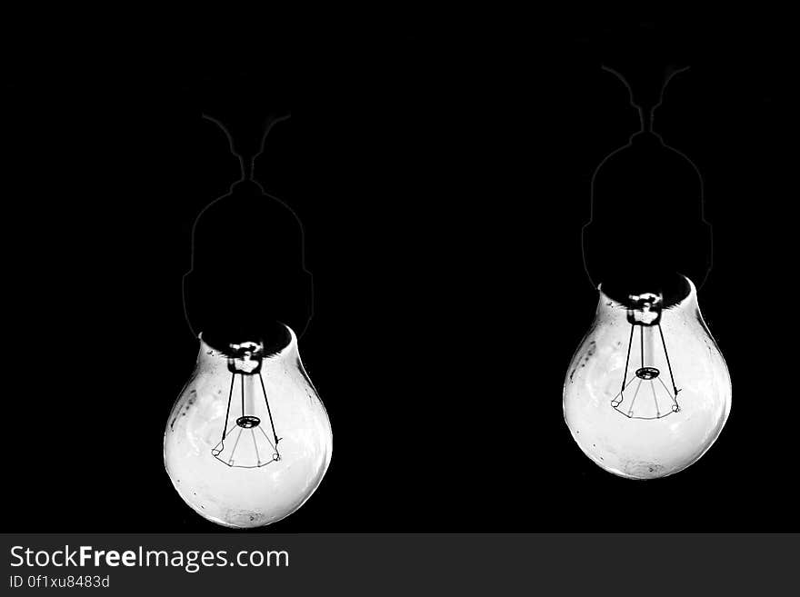 Closeup of two bright retro style filament bulbs with sockets and wires just visible on a black background. Closeup of two bright retro style filament bulbs with sockets and wires just visible on a black background.