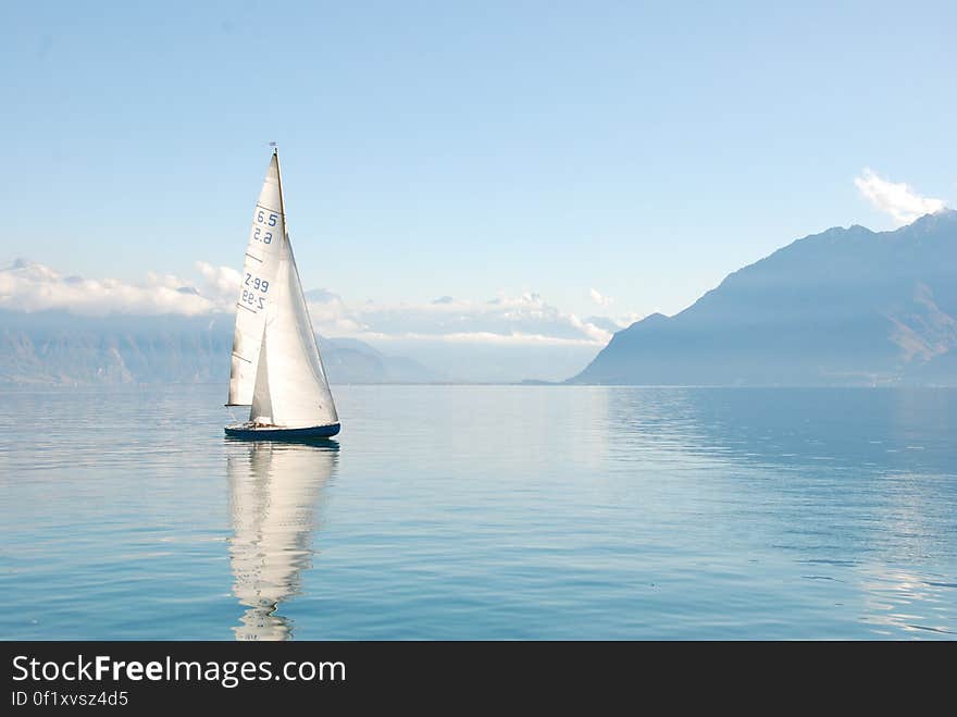 A sailboat in a bay reflecting on the water surface. A sailboat in a bay reflecting on the water surface.