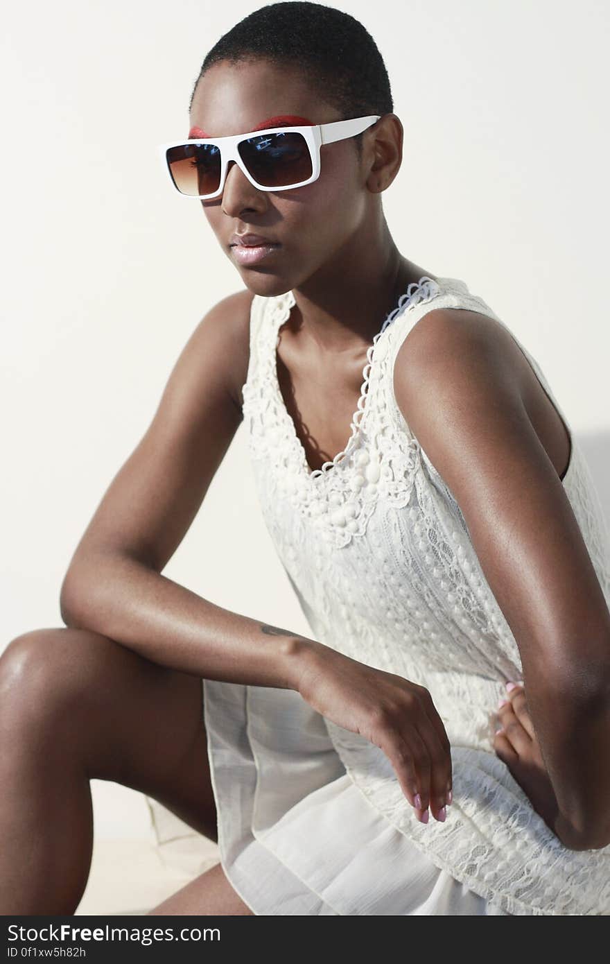 Woman Wearing White Tank Dress and White Frame Sunglasses Sitting and Making a Pose