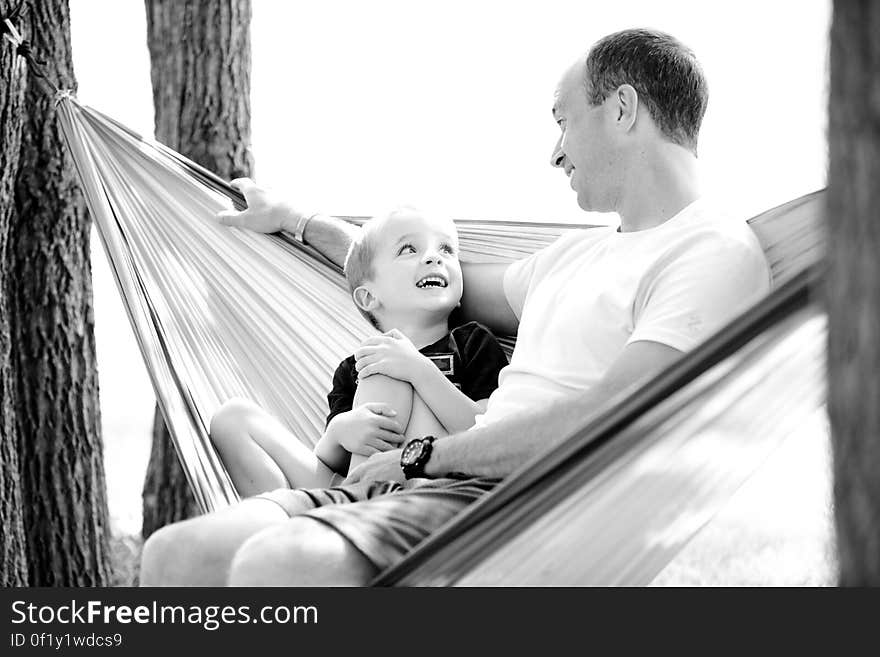 A black and white photo of a father and his son sitting in a hammock looking at each other and smiling. A black and white photo of a father and his son sitting in a hammock looking at each other and smiling.