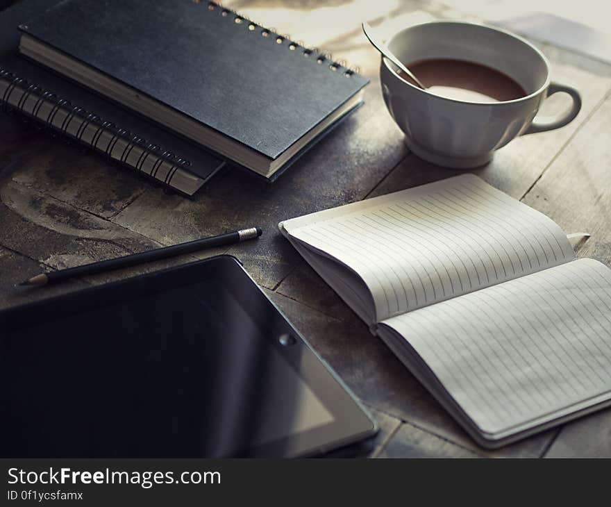 A table with opened journal, cup of coffee and a tablet. A table with opened journal, cup of coffee and a tablet.