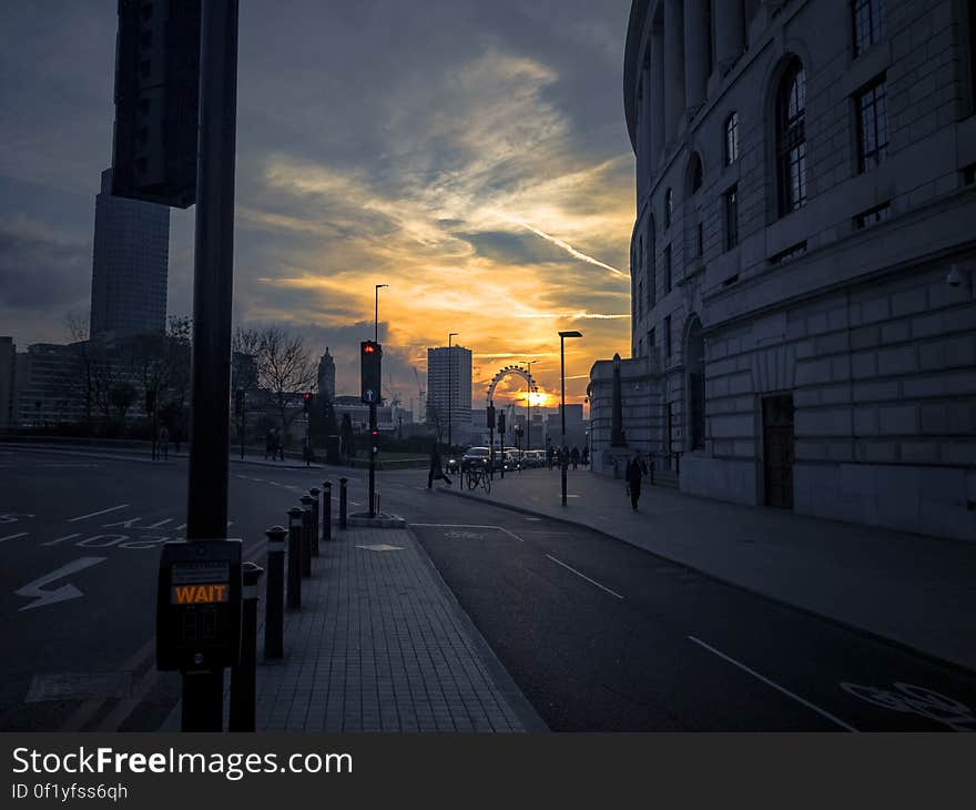 London street at sunset with historic stone building on the right and London Eye in the distance highlighted by a golden sky.