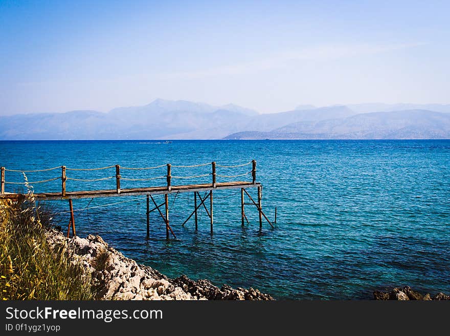 A small wooden pier on in the water with mountains on the distance.