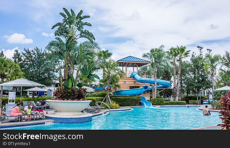 A view from a tropical resort with swimming pool, slide and sun chairs.