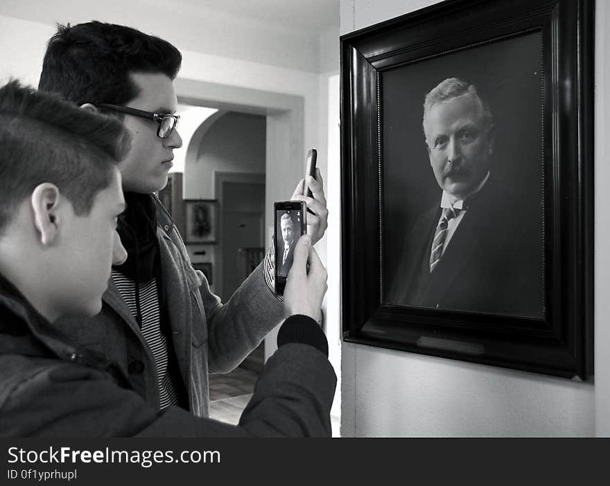 A pair of men taking a photo of a painting with smartphone. A pair of men taking a photo of a painting with smartphone.