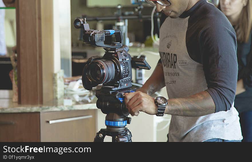 A photographer setting up a video camera on tripod.