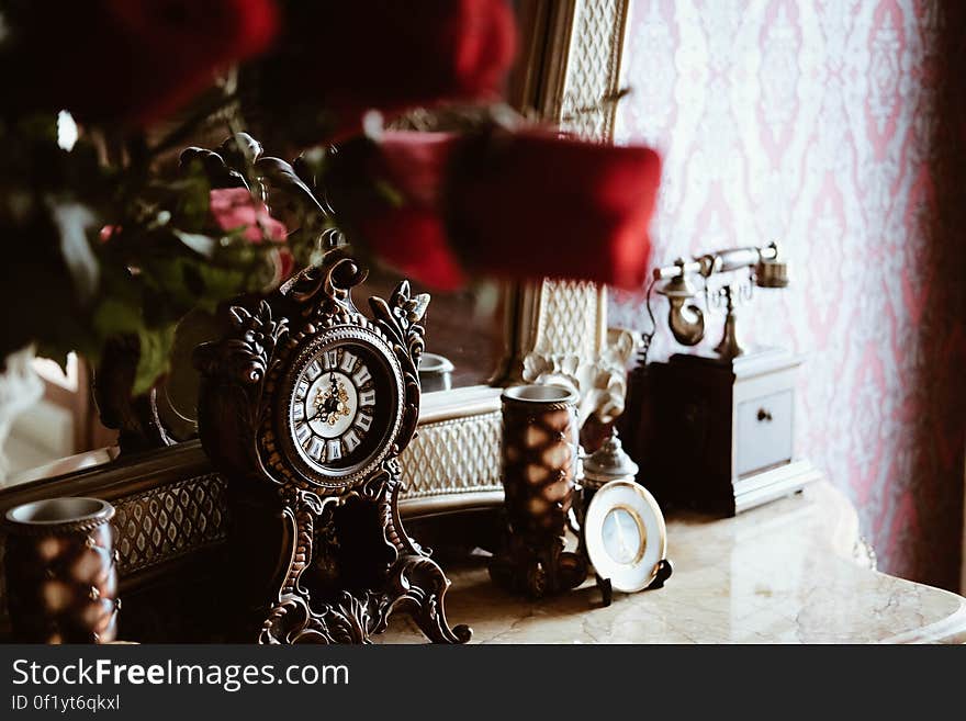 A side table with a mirror and antique phone and clock. A side table with a mirror and antique phone and clock.