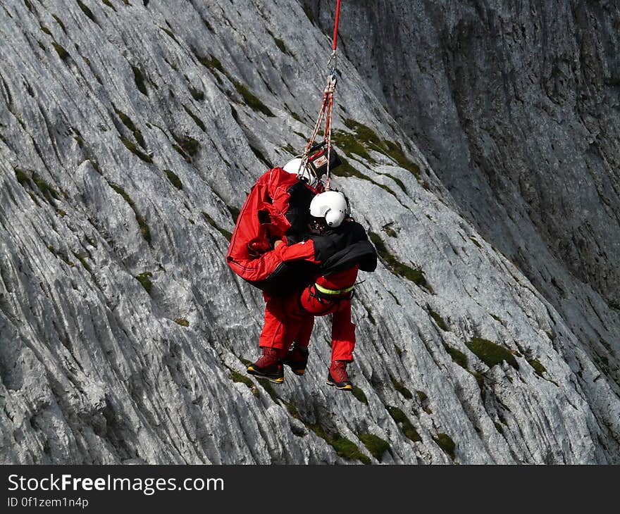 A rescue operation with an operator lifting another person on a cable hanging from a helicopter. A rescue operation with an operator lifting another person on a cable hanging from a helicopter.