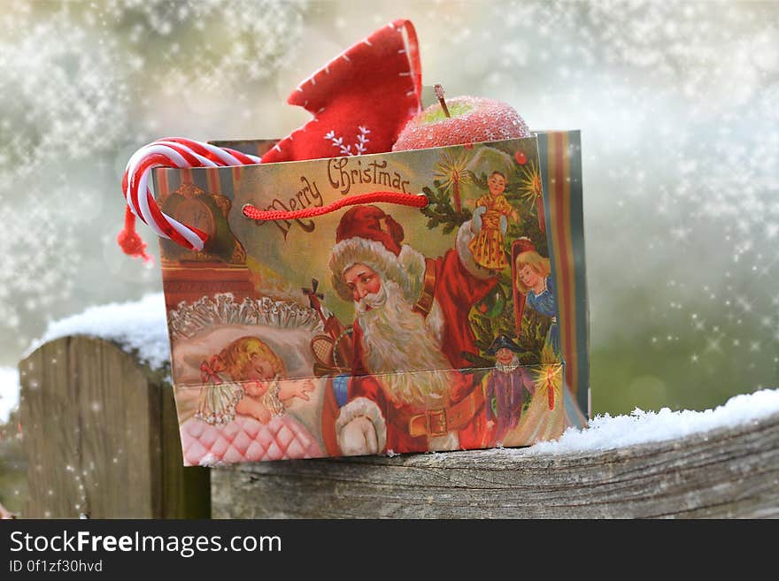 A Christmas gift bag with sweets and fruits on a snowy fence.