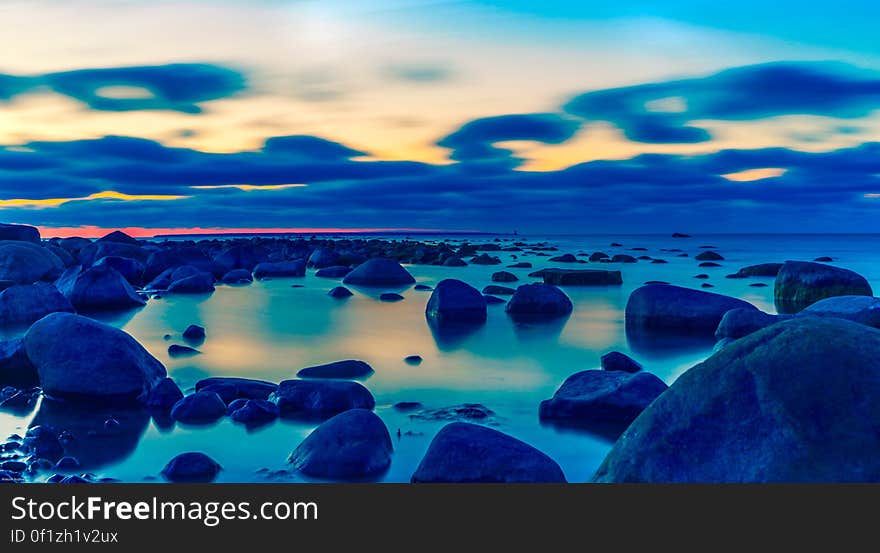 Rocky beach at dusk, sky colors and clouds reflecting on the water surface.