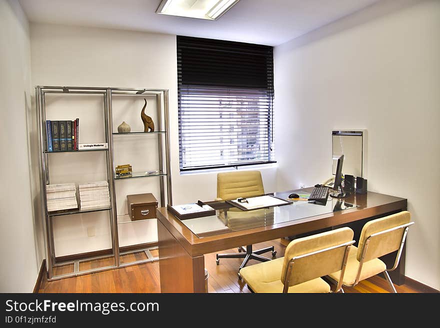 Light, bright office or consulting room with desk and three chairs, window with Venetian blinds and modern bookcase.