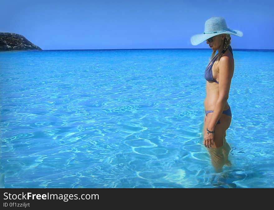 Portrait of woman in bikini with sunhat standing in blue waters on coastline. Portrait of woman in bikini with sunhat standing in blue waters on coastline.