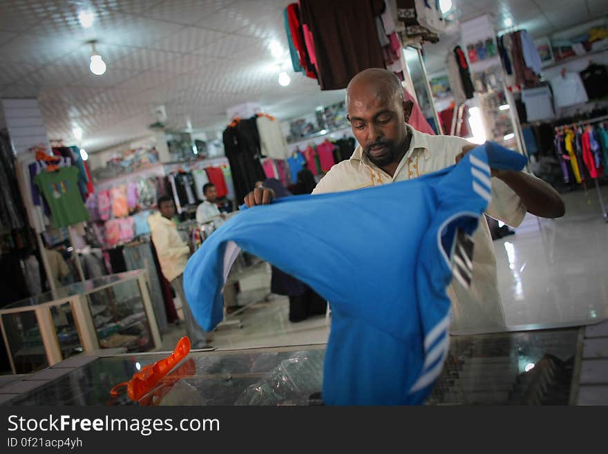 A sales attendent folds a football shirt in a clothing and footwear shop in Hamar Weyne market in the Somali capital Mogadishu, 05 August, 2013. 06 August marks 2 years since the Al Qaeda-affiliated extremist group Al Shabaab withdrew from Mogadishu following sustained operations by forces of the Somali National Army &#x28;SNA&#x29; backed by troops of the African Union Mission in Somalia &#x28;AMISOM&#x29; to retake the city. Since the group&#x27;s departure the country&#x27;s captial has re-established itself and a sense of normality has returned. Buildings and infrastructure devastated and destroyed by two decades of conflict have been repaired; thousands of Diaspora Somalis have returned home to invest and help rebuild their nation; foreign embassies and diplomatic missions have reopened and for the first time in many years, Somalia has an internationally recognised government.. AU-UN IST PHOTO / STUART PRICE. A sales attendent folds a football shirt in a clothing and footwear shop in Hamar Weyne market in the Somali capital Mogadishu, 05 August, 2013. 06 August marks 2 years since the Al Qaeda-affiliated extremist group Al Shabaab withdrew from Mogadishu following sustained operations by forces of the Somali National Army &#x28;SNA&#x29; backed by troops of the African Union Mission in Somalia &#x28;AMISOM&#x29; to retake the city. Since the group&#x27;s departure the country&#x27;s captial has re-established itself and a sense of normality has returned. Buildings and infrastructure devastated and destroyed by two decades of conflict have been repaired; thousands of Diaspora Somalis have returned home to invest and help rebuild their nation; foreign embassies and diplomatic missions have reopened and for the first time in many years, Somalia has an internationally recognised government.. AU-UN IST PHOTO / STUART PRICE.