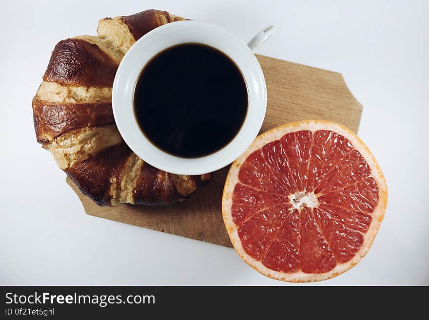 A croissant, a cup of coffee and a half of red grapefruit. A croissant, a cup of coffee and a half of red grapefruit.