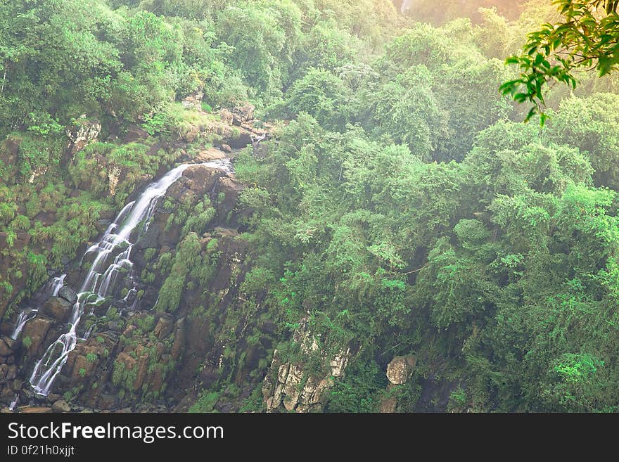 Waterfall down several rock pathways and cliff set in a green forest on a bright sunny day. Waterfall down several rock pathways and cliff set in a green forest on a bright sunny day.