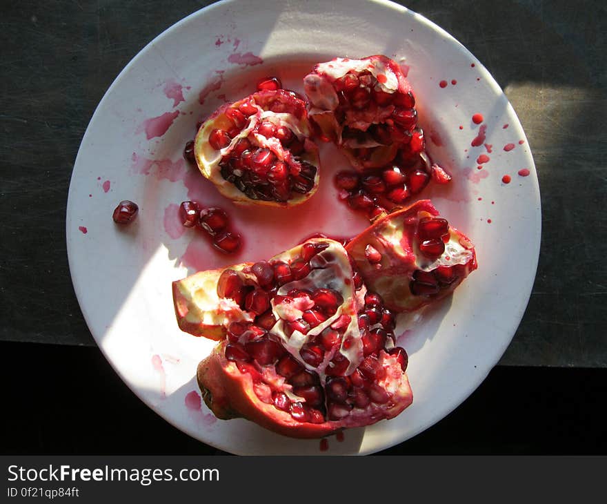 Pomegranate fruit on a white plate open with seeds visible and red spots every where, mainly dark background. Pomegranate fruit on a white plate open with seeds visible and red spots every where, mainly dark background.