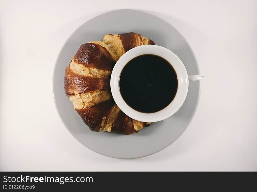 A cup of coffee with a fresh croissant. A cup of coffee with a fresh croissant.