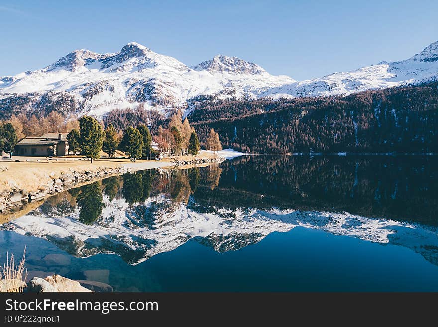 A lake in the valley with house on the shore and snowy mountain peaks in the background. A lake in the valley with house on the shore and snowy mountain peaks in the background.