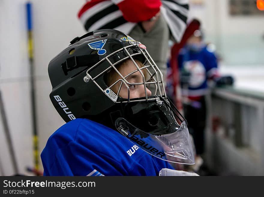 Young hockey player sitting on bench next to rink wearing helmet during match.