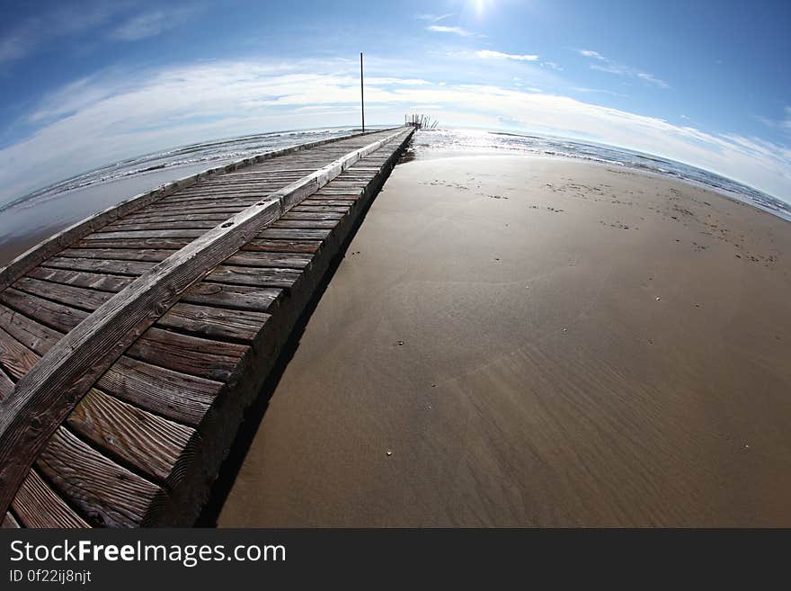 Fish eye view of wooden pier on beach with sea and blue sky in background.