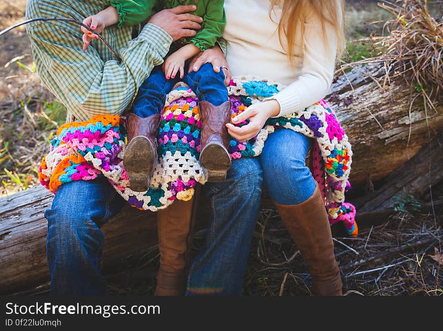 The parents holding a child and sitting outdoors on a log with a colorful quilt. The parents holding a child and sitting outdoors on a log with a colorful quilt.