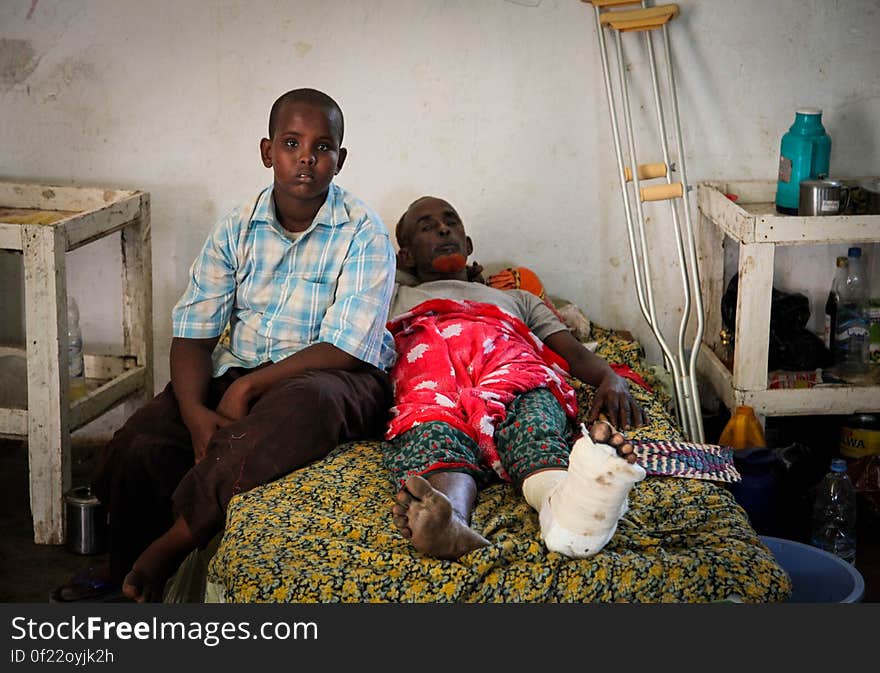 SOMALIA, Kismayo: In a photograph taken 15 July 2013 and released by the African Union-United Nations Information Support Team 22 July, a man injured during recent fighting in Kismayo is seen with his son on a bed inside Kismayo hospital in southern Somalia. during a visit by members of the African Union Mission in Somalia &#x28;AMISOM&#x29;. AU-UN IST PHOTO / RAMADAN MOHAMED HASSAN. SOMALIA, Kismayo: In a photograph taken 15 July 2013 and released by the African Union-United Nations Information Support Team 22 July, a man injured during recent fighting in Kismayo is seen with his son on a bed inside Kismayo hospital in southern Somalia. during a visit by members of the African Union Mission in Somalia &#x28;AMISOM&#x29;. AU-UN IST PHOTO / RAMADAN MOHAMED HASSAN.