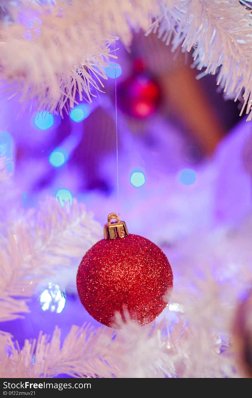 Red bauble on Christmas tree with white branches and lights in background.