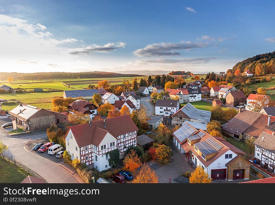 Small country village with attractive modern houses, some mock Tudor and bungalows with solar panels with lots of trees in Autumnal colors, blue sky and cloud background. Small country village with attractive modern houses, some mock Tudor and bungalows with solar panels with lots of trees in Autumnal colors, blue sky and cloud background.