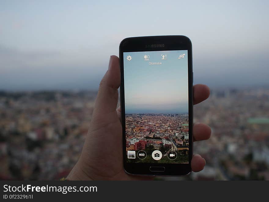 Person Holding a Black Samsung Galaxy Android Smartphone Taking a Picture of Cityscape over Blue and White Sky during Daytime