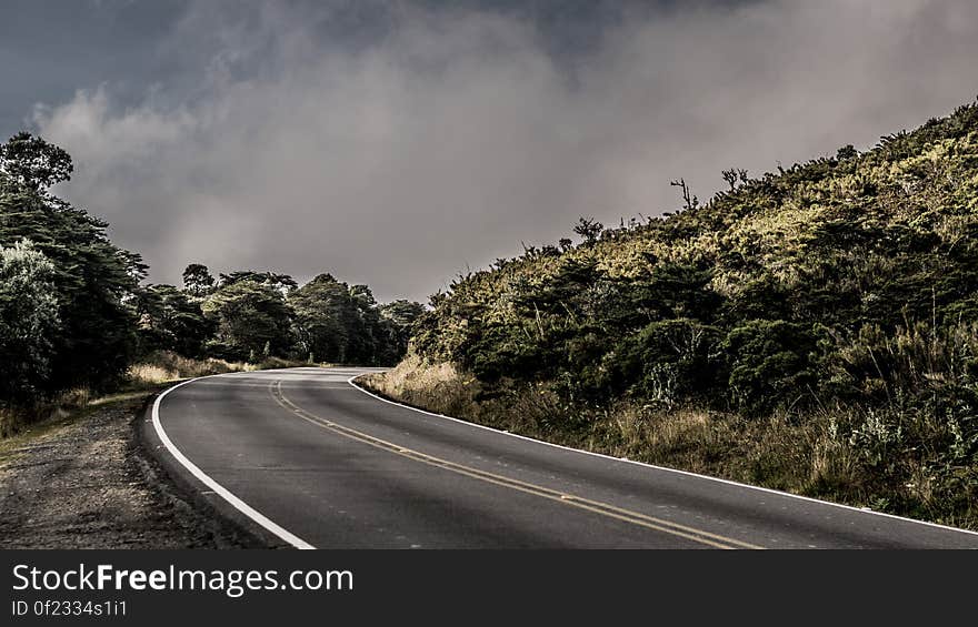 An asphalt road passing through a green hilly landscape.