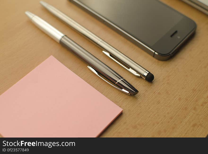 A mobile phone with sticky notes and a pair of pens. A mobile phone with sticky notes and a pair of pens.