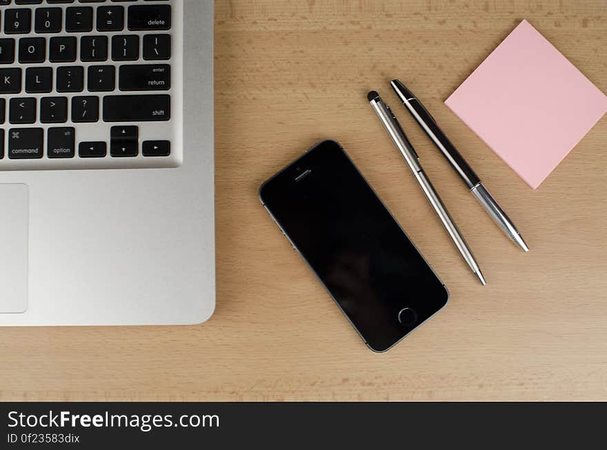 A laptop computer with a smartphone, pens and sticky notepad for keeping notes. A laptop computer with a smartphone, pens and sticky notepad for keeping notes.