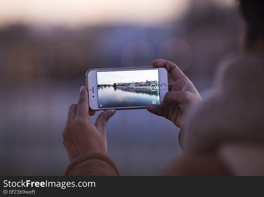 A person photographing a river and city view with a smartphone camera. A person photographing a river and city view with a smartphone camera.