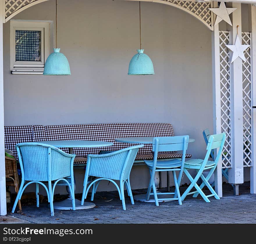 Café with four blue chairs and a chequered bench seat in a small alcove with tables and matching blue light shades overhead and cobbled floor below. Café with four blue chairs and a chequered bench seat in a small alcove with tables and matching blue light shades overhead and cobbled floor below.