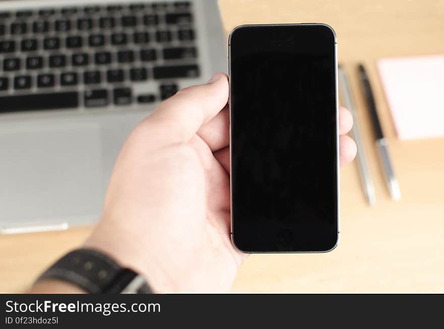 A person holding a smartphone on his hand with laptop computer on the background. A person holding a smartphone on his hand with laptop computer on the background.