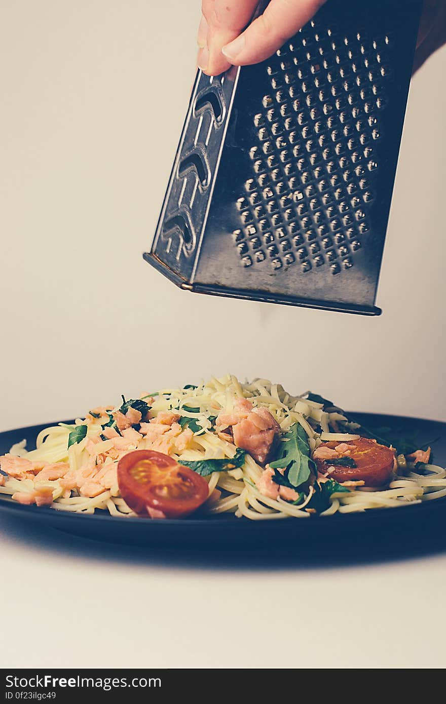 Person grating cheese on top of plate of pasta with vegetables.