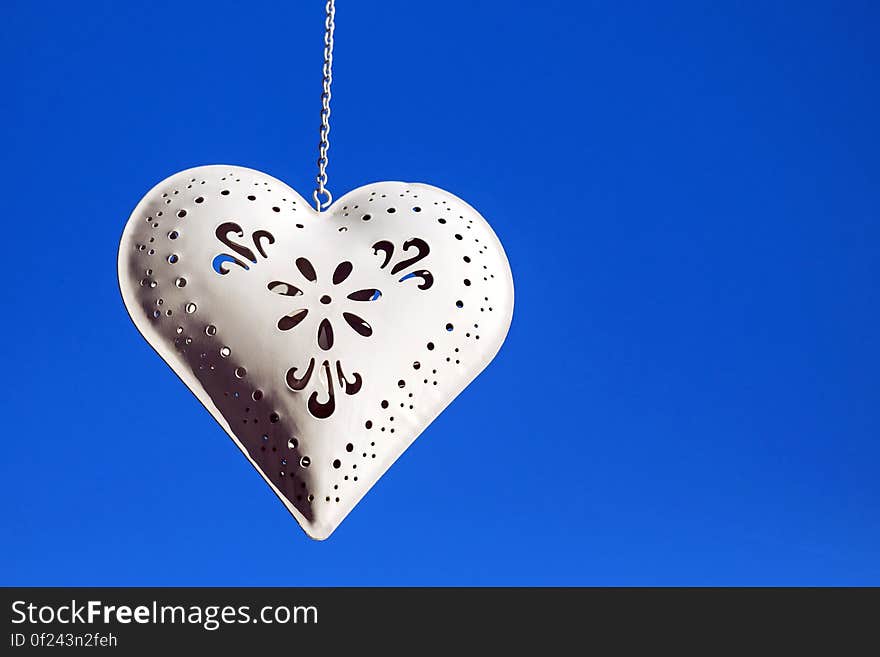 A white decorative metal heart hanging from a chain.