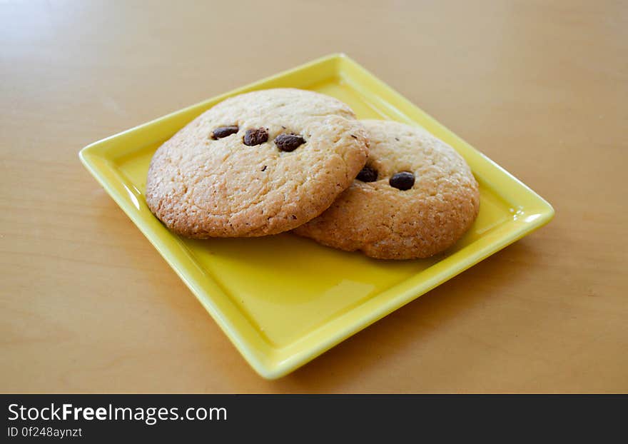 Two freshly baked chocolate chip biscuits on yellow plate.