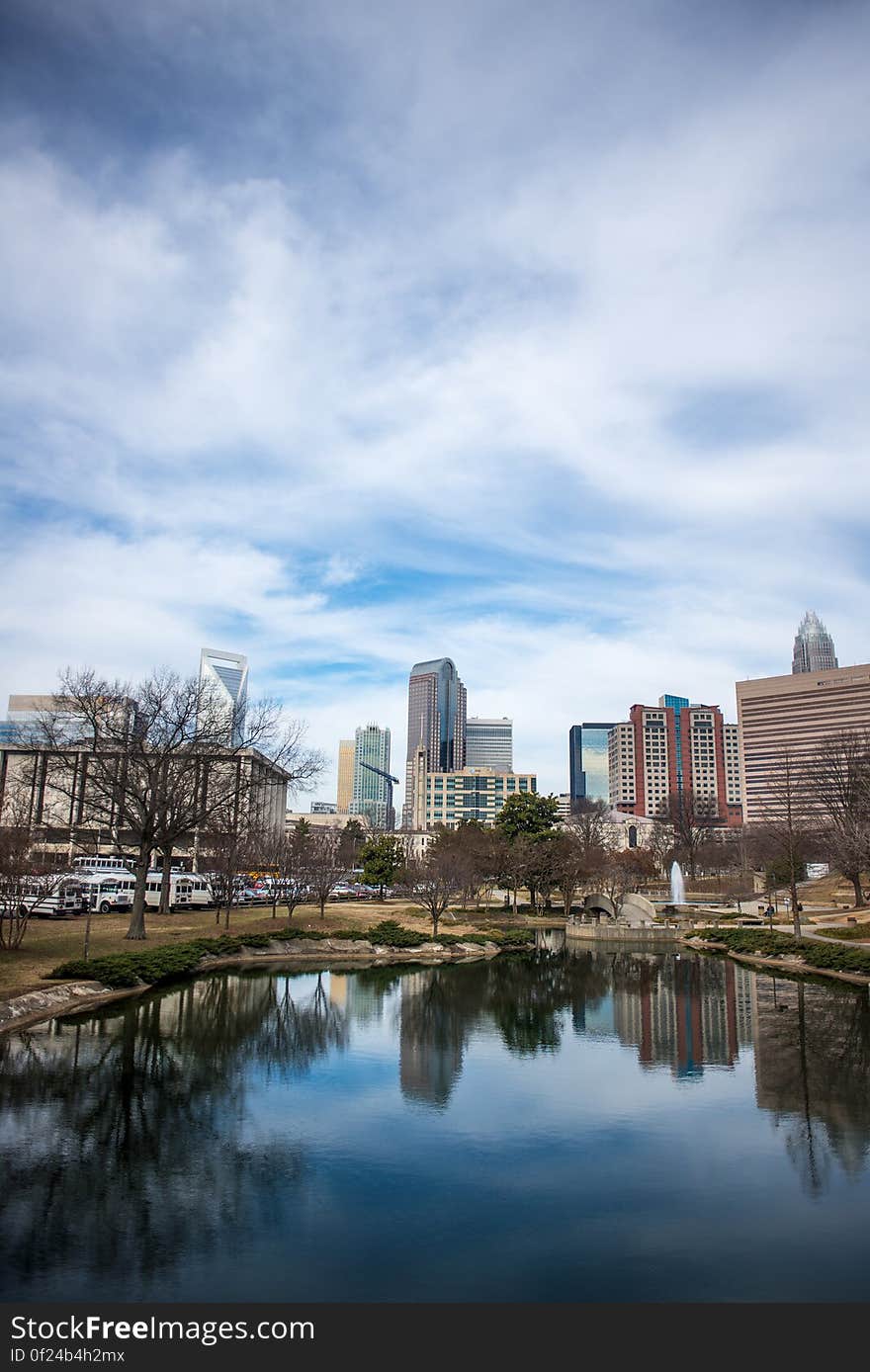 Park trees and buildings reflecting on lake in modern city with cloudscape background. Park trees and buildings reflecting on lake in modern city with cloudscape background.