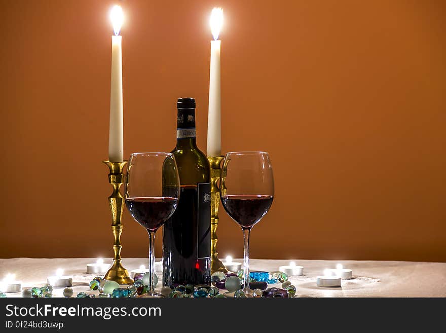 Wine glasses with bottle and lighted candles on romantic dinner setting with gem stones. Wine glasses with bottle and lighted candles on romantic dinner setting with gem stones.